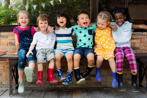 i bambini dell'asilo amici armano in giro seduti sorridenti - child playing multi ethnic group summer foto e immagini stock