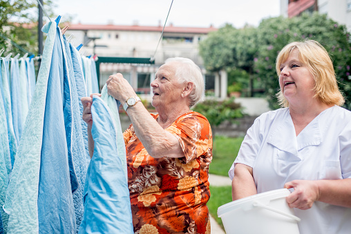 Senior Woman  With The Help Of Nurse Hanging Laundry At The Backyard Of The Nursing Home