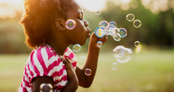 fille d’ascendance africaine jouant la bulle de soufflage dans un parc - fun enjoyment children only pre adolescent child photos et images de collection