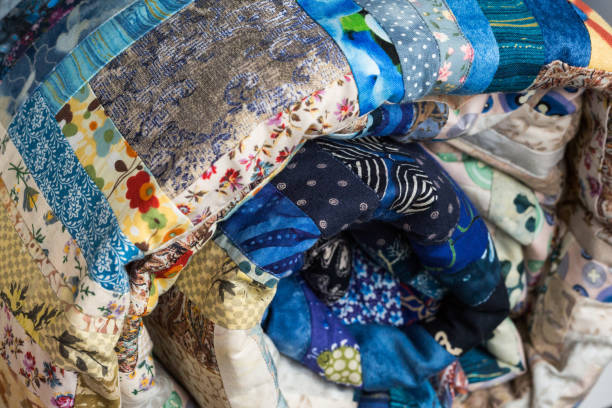 istock sewing, patchwork and fashion concept - macro of bright blue beautiful multi-colored quilted blanket rolled up in the tube, warehouse of finished needlework products, side view 685868858