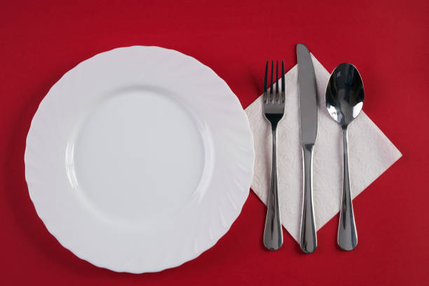 istock Empty white dinner plate with silver fork and Dessert Tablespoon, isolated on red tablecloth background with copy space. Table Setting, Folded Napkin. Dinner place setting 685871578