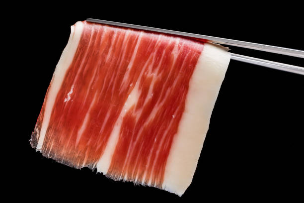 Piece of cured ham on tweezer. Extreme macro close up of cut piece of cured Spanish bellota pork ham on tweezer. caterer photos stock pictures, royalty-free photos & images