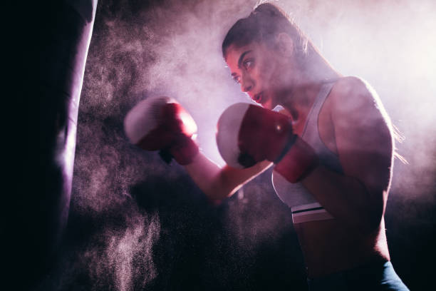 jovem mulher treinando com luvas de boxe e um saco de pancadas - muay thai kickboxing women martial arts - fotografias e filmes do acervo