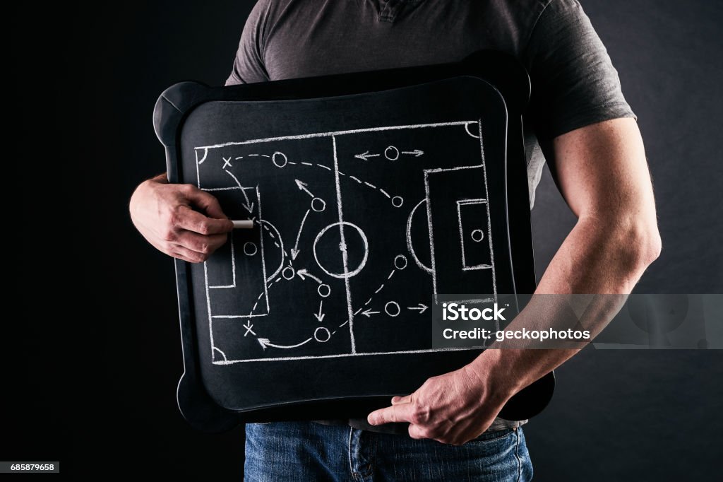 Hand of a football or soccer play coach drawing a tactics of football game with white chalk on blackboard at changing room during the time out Sports Playbook Stock Photo