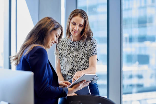 istock Business professionals are discussing in creative office. Female executive is pointing at digital tablet to colleague against window. They are wearing smart casuals. 685888036