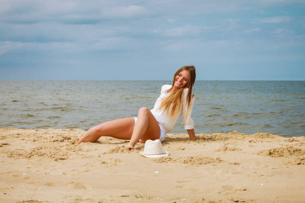Blonde woman sitting on the sand on the beach.