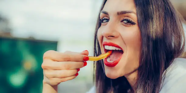 Photo of Woman eating french fries potato with ketchup in a restaurant