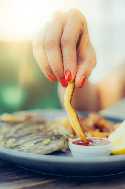 Photo of Woman eating french fries potato with ketchup in a restaurant