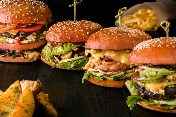 Assorted burgers with different fillings, with sesame seeds on wooden table isolated on black background Assorted burgers with different fillings, with sesame seeds on wooden table isolated on black background. Bar menu onion dome stock pictures, royalty-free photos & images