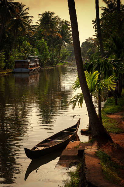 A canoe parked at sides of backwater canal on a partial cloudy afternoon at Alleppey in Kerala stock photo