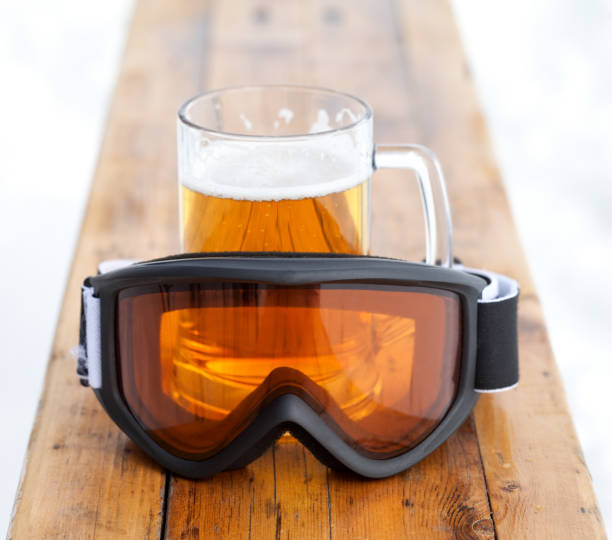 Ski goggles and glass mug with fresh cold beer on wooden bench in outdoor cafe at ski resort