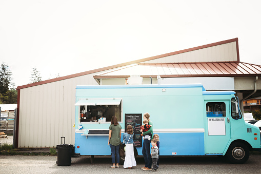 A young family group shares fun food and memories at a local food cart, serving delicious handmade sandwiches and snacks.  Here the look at the menu, trying to decide what they'd like to order.