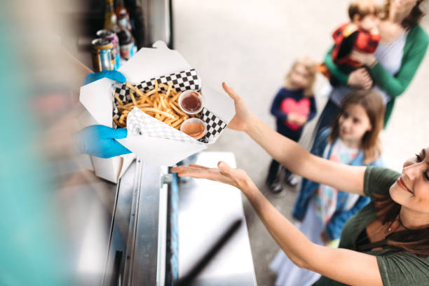 Woman Receiving Order at Food Truck A young family group shares fun food and memories at a local food cart, serving delicious handmade sandwiches and snacks.  One of the women smiles as she receives her order of gourmet french fries with special dipping sauce. concession stand stock pictures, royalty-free photos & images