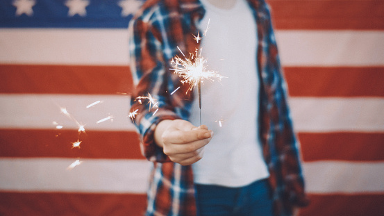 boy in front of american flag holding sparkler in hand