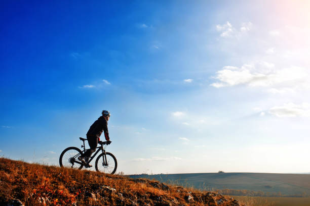 istock Cyclist riding his bike down on mountain trail. Beautiful sky and clouds on background 686020708