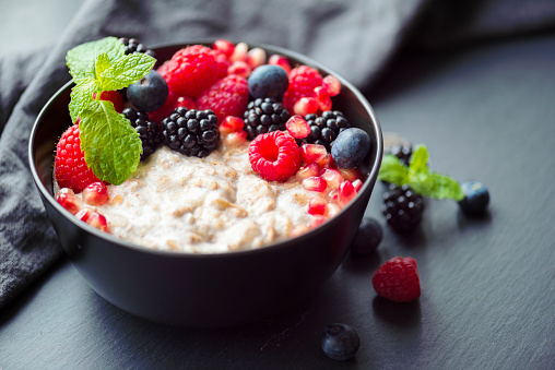 Healthy organic breakfast porridge topped with raspberries, blackberries, blueberries, and mint leaves