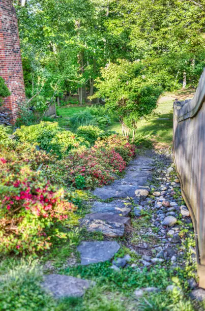 Private garden path with stones and red flowers and fence