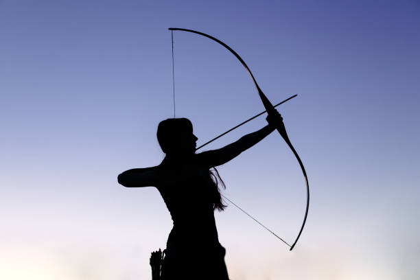 archer de mujer pelo jengibre disparos blancos con su arco y flecha. concentración, destino, éxito concepto - bow and arrow fotografías e imágenes de stock