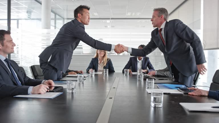 Asian and Caucasian businessman shaking hands in front of their project teams in the conference room