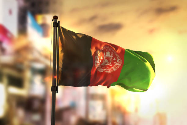 afghanistan flag against city blurred background at sunrise backlight - flag of afghanistan imagens e fotografias de stock