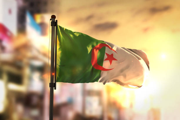 Algeria Flag Against City Blurred Background At Sunrise Backlight Algeria Flag Against City Blurred Background At Sunrise Backlight algeria flag silhouettes stock pictures, royalty-free photos & images
