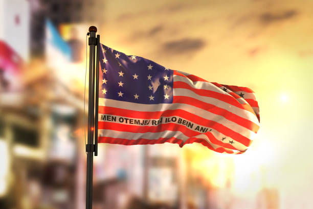 Bikini Atoll Flag Against City Blurred Background At Sunrise Backlight