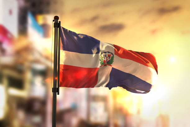 доминиканская республика флаг против города размыты фон на восходе подсветки - dominican flag стоковые фото и изображения