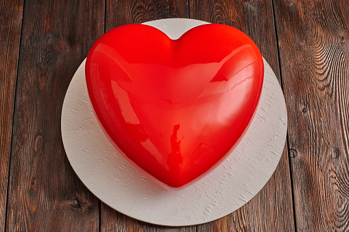 Red glaze mousse cake, heart shape form on wooden background, closeup