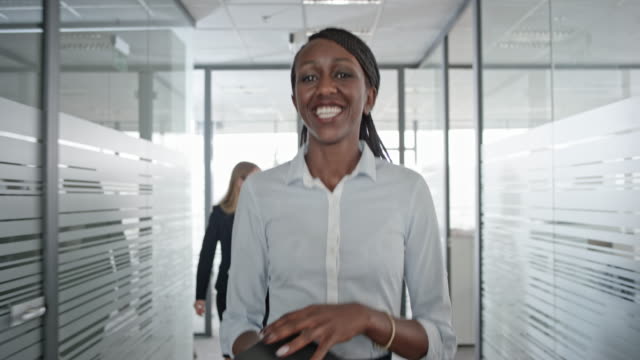 African-American female office employee smiling as she walks down the office hallway