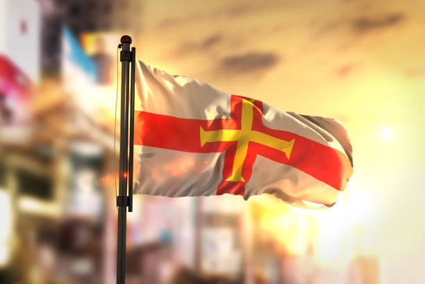 Guernsey Flag Against City Blurred Background At Sunrise Backlight Guernsey Flag Against City Blurred Background At Sunrise Backlight guernsey city stock pictures, royalty-free photos & images