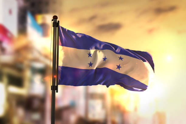 drapeau du honduras contre ville floue fond à rétro-éclairage de sunrise - central america flash photos et images de collection