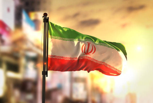 bandera de irán contra la ciudad borrosa de fondo en contraluz amanecer - iranian flag fotografías e imágenes de stock