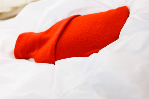 istock Warm red hot water bottle on white bedding 686174112