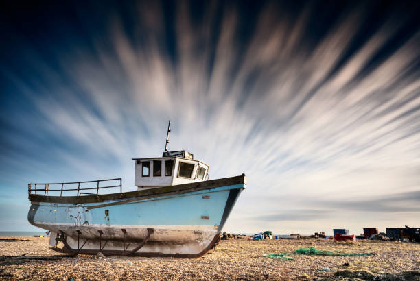 istock Old fishing boat stranded on a pebbled beach with dramatic long-exposure sky. Dungeness, England 686174388
