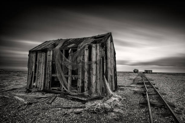 Abandoned fisherman's hut on a pebble beach with long exposure clouds in monochrome. Dungeness, England