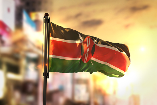 Kenya Flag Against City Blurred Background At Sunrise Backlight
