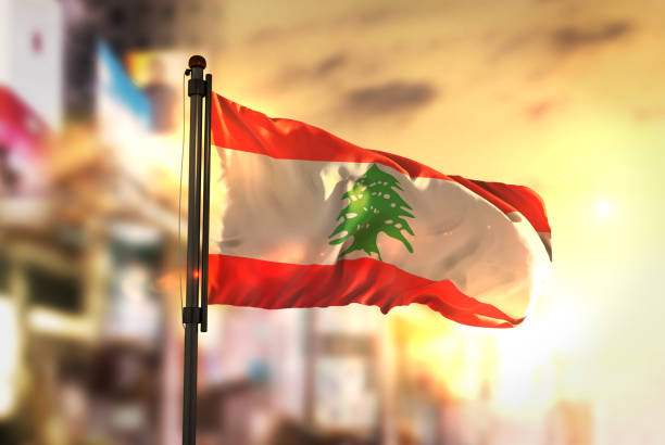 市に対してレバノンの国旗日の出バックライトで背景がぼやけてください。 - lebanese flag ストックフォトと画像