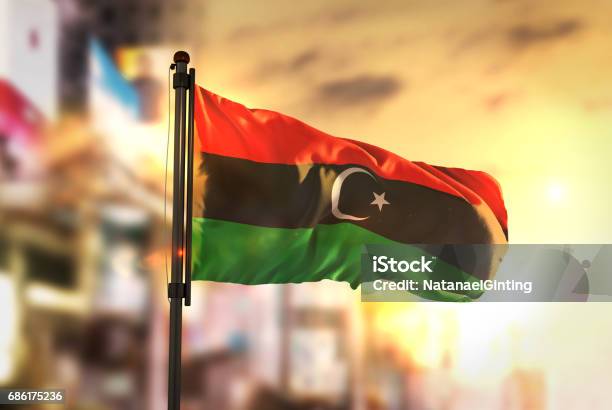 Libya Flag Against City Blurred Background At Sunrise Backlight Stock Photo - Download Image Now