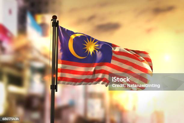 Malaysia Flag Against City Blurred Background At Sunrise Backlight Stock Photo - Download Image Now