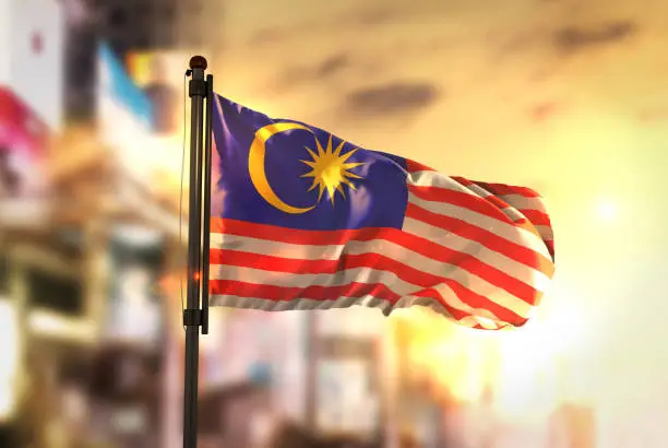 Malaysia Flag Against City Blurred Background At Sunrise Backlight