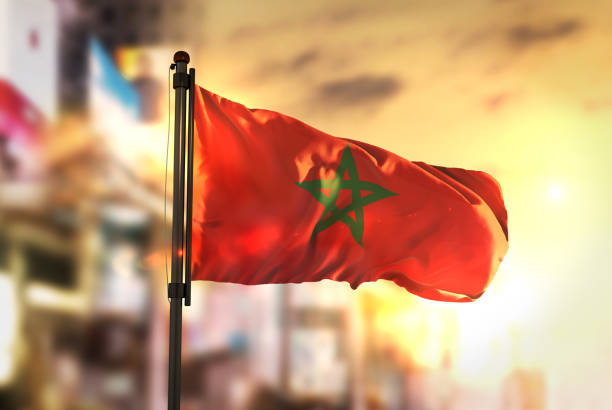 marokko flagge gegen city unscharf hintergrund bei sonnenaufgang hintergrundbeleuchtung - moroccan flags stock-fotos und bilder