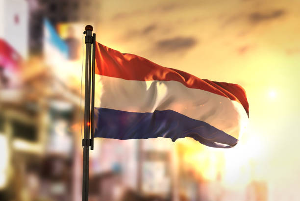 Netherlands Flag Against City Blurred Background At Sunrise Backlight