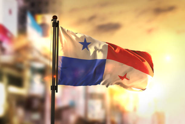 drapeau du panama contre le ville floue fond à rétro-éclairage de sunrise - central america flash photos et images de collection