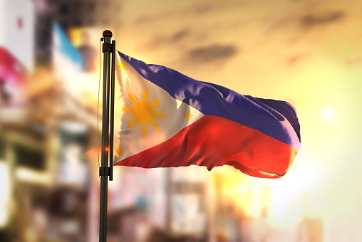 Philippines Flag Against City Blurred Background At Sunrise Backlight