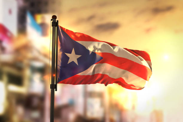 bandera de puerto rico contra la ciudad borrosa de fondo en contraluz amanecer - puerto rico fotografías e imágenes de stock