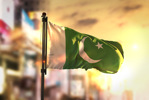 Pakistan Flag Against City Blurred Background At Sunrise Backlight