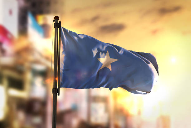 Somalia Flag Against City Blurred Background At Sunrise Backlight