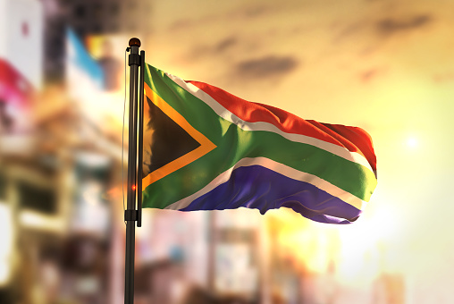 South Africa Flag Against City Blurred Background At Sunrise Backlight