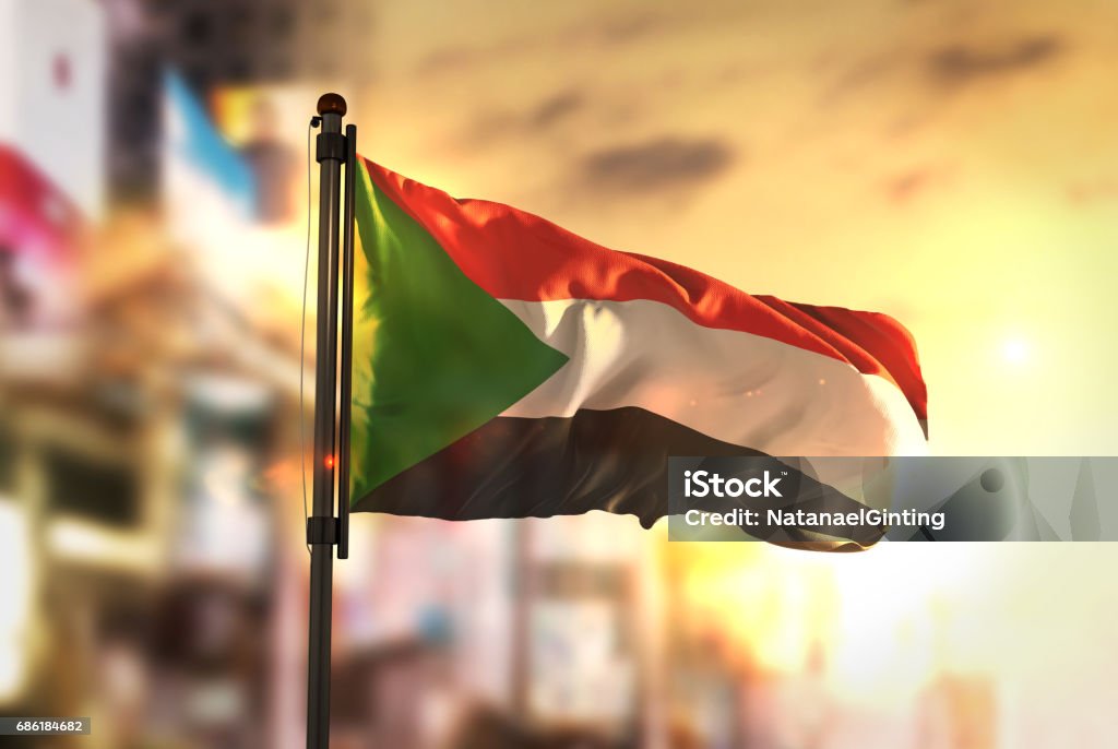 Sudan Flag Against City Blurred Background At Sunrise Backlight Sudan Stock Photo