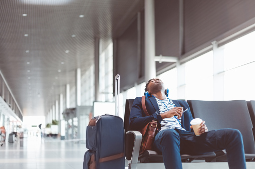 Young african man sitting at airport lounge and sleeping, waiting for flight at airport departure area.